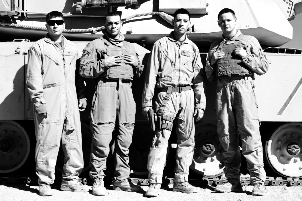 Four U.S. Marine tank crew members standing together in front of their M1A1 Abrams tank — Heavy Metal Brotherhood